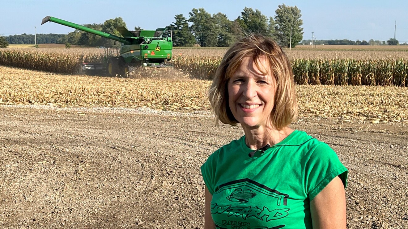 A photo of Christie Wilson, a lifelong farmer, standing in a field in front of a tractor.