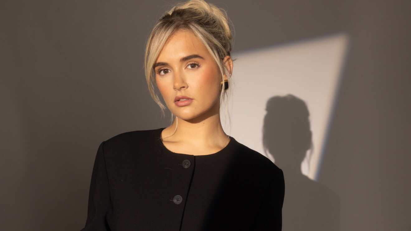 Young blonde woman in black jacket, dramatic lighting with shadow
