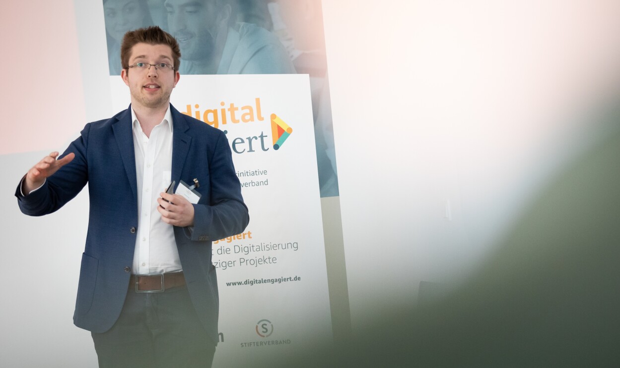 Daniel Stark steht vor einem digital.engagiert-Poster und gestikuliert