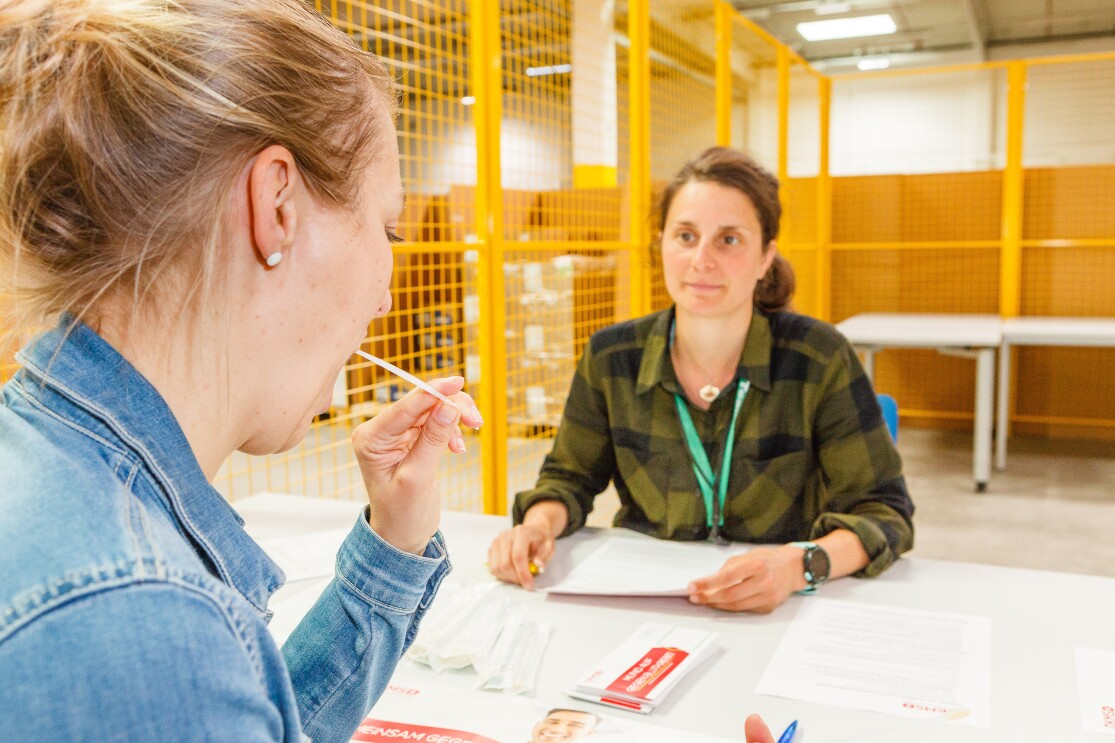 Eine blonde Mitarbeiter lässt sich typisieren - vor ihr hält eine weitere Mitarbeiterin die DKMS-Formulare bereit