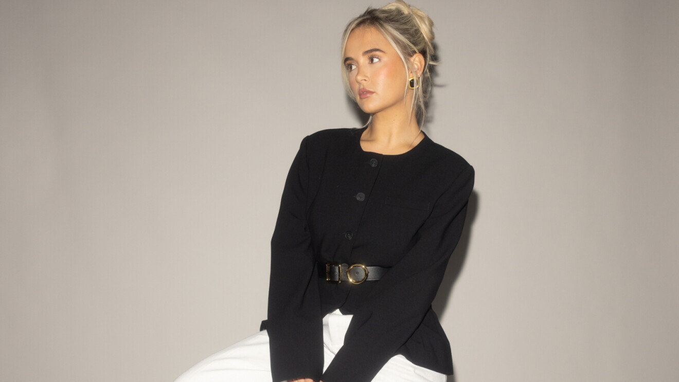 Blonde woman in black top with belt, looking sideways