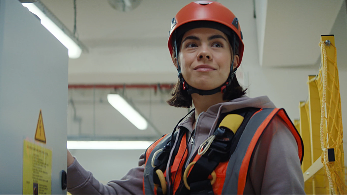 Foto aus der aktuellen Amazon Kampagne: Zu sehen ist das Porträt einer jungen Amazon Technikerin. Sie trägt eine orangene Sicherheitsweste und Helm.