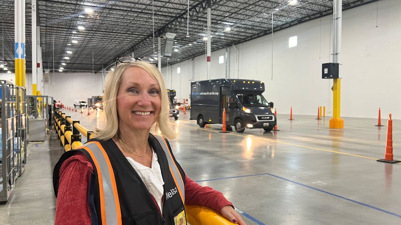 An image of a woman, an Amazon Delivery Service Partner, in a work vest standing in front of a delivery van.