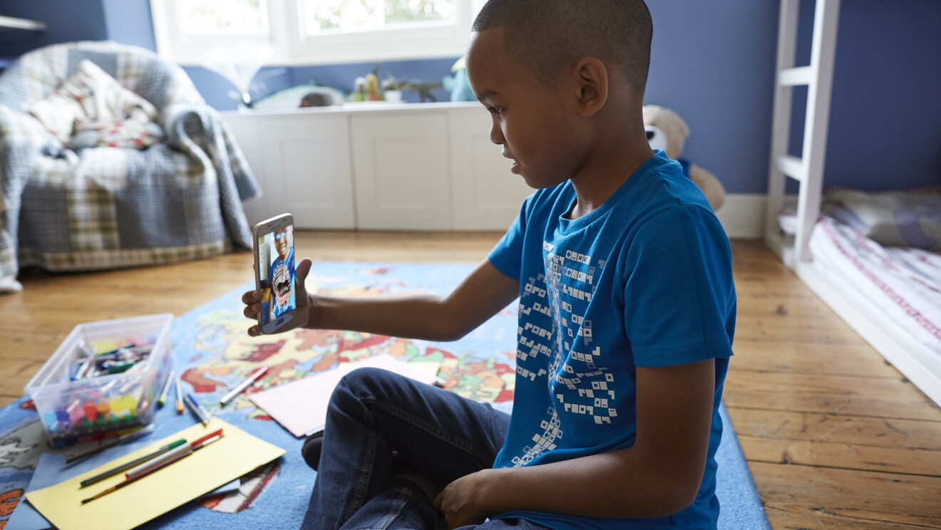 Bambino seduto in una stanza da gioco si inquadra con il suo smartphone mentre indossa una t-shirt Curiscope e sullo schermo appare una ricostruzione dei suoi organi interni.