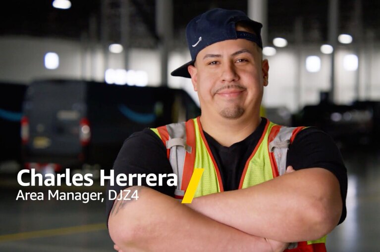 Charles stands with his arms crossed and smiles in an Amazon fulfillment center.