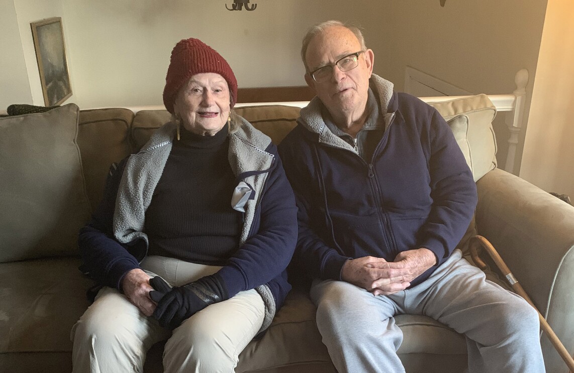 An image of a man and a woman sitting on a couch in their home, smiling for a photo.