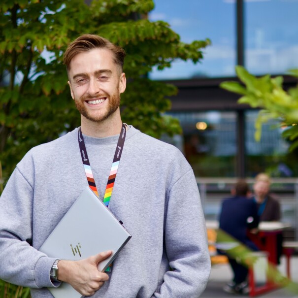 Smiling person holding HP laptop outdoors with rainbow lanyard
