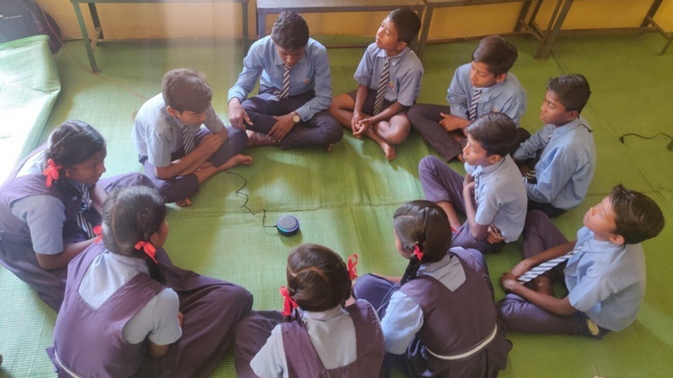 A bunch of school children surrounding an Echo device. 