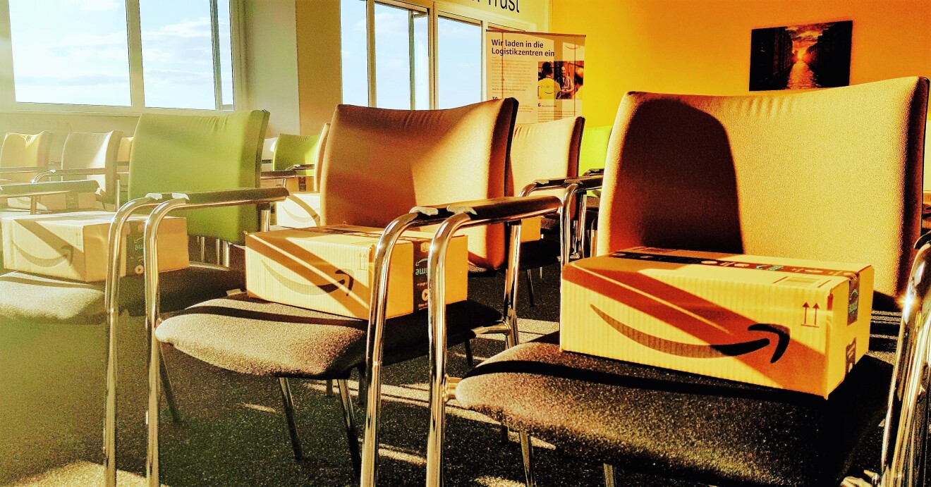 Ein lichtdurchfluteter Konferenzraum mit Stühlen: Auf jedem Platz liegt ein Amazon Päckchen. Gut sichbar: der Amazon Smile Pfeil