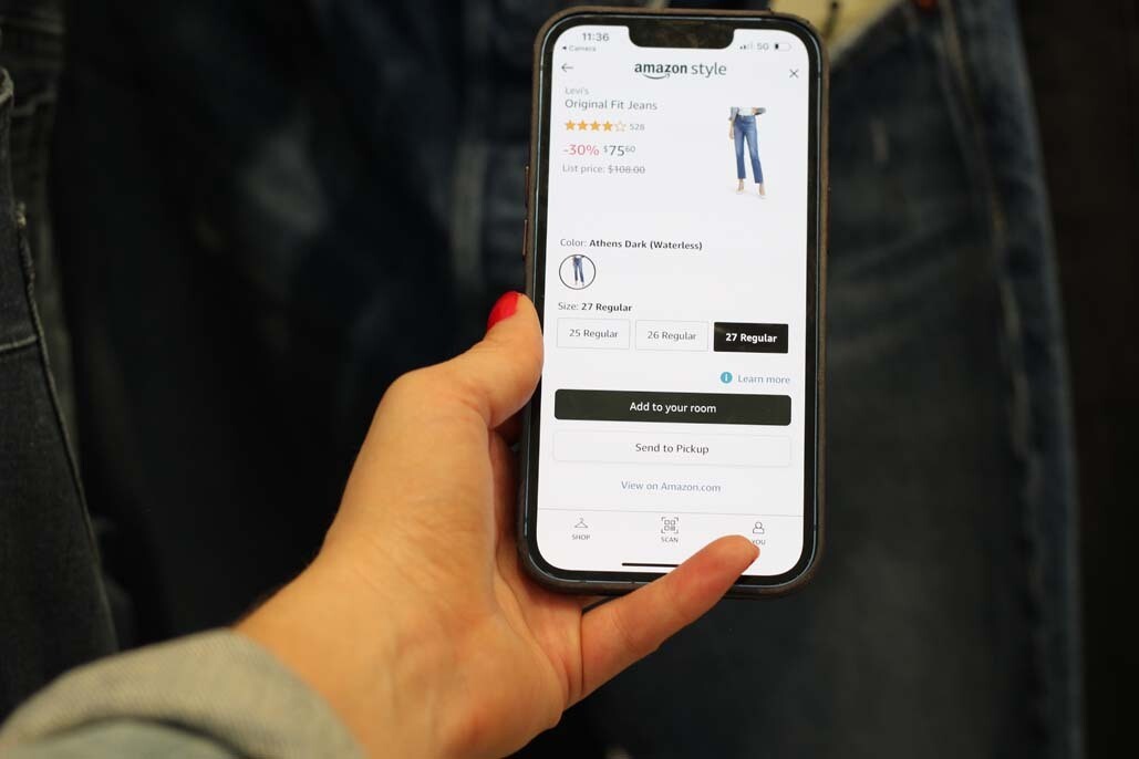 A hand is holding a phone. On the screen you see the detail page for a pair of jeans on Amazon.com