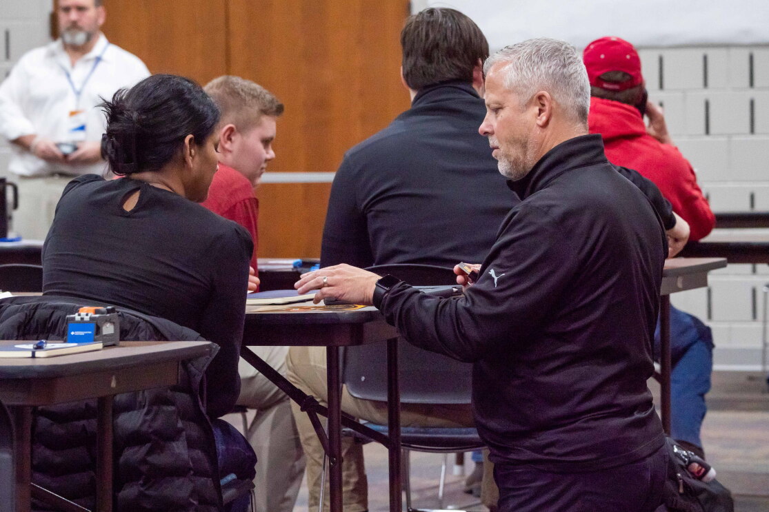 Craig Mathes, VP of Safety and Human Resources at Team Fishel, kneeling and helping a student