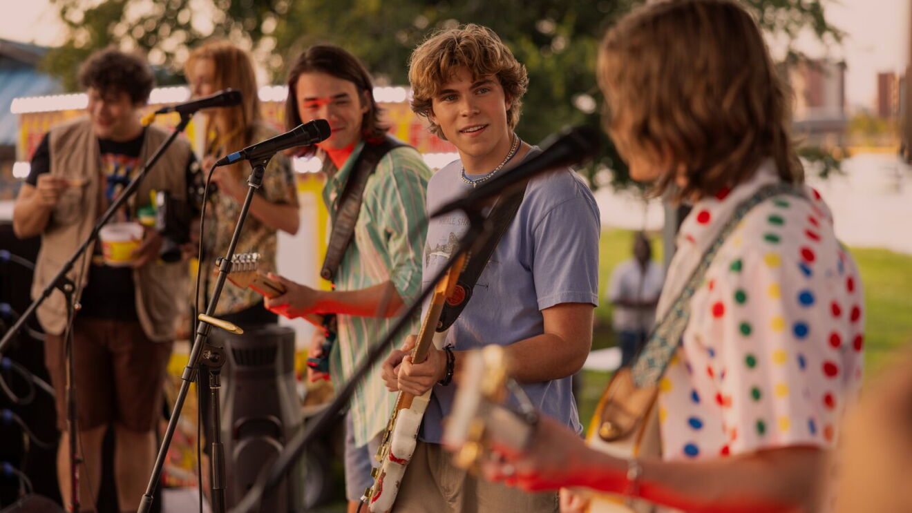 A scene from The Runarounds with a teenage band performing outdoors with guitars and microphones