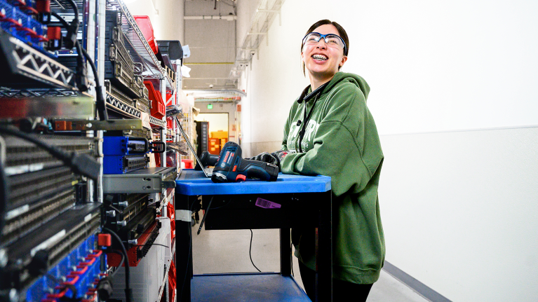 A data center technician working on their laptop in front of servers.
