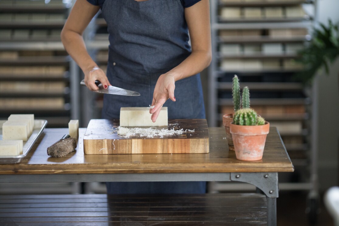 An employee at Little Flower Soap Company cuts a block of soap by hand, to create bars of soap to be packaged and shipped to customers. 