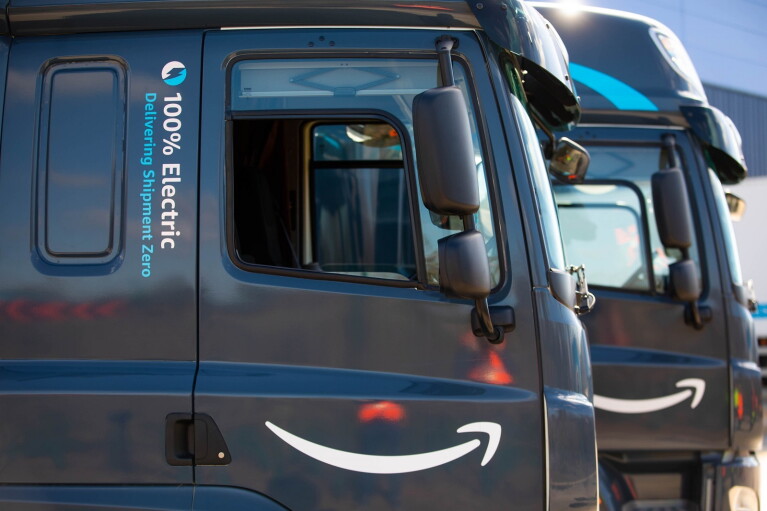 Zwei voll elektrische LKWs mit Amazon Branding sind hintereinander Stehend zu sehen.