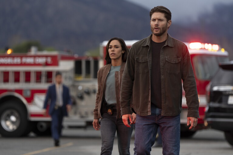 A still from Countdown, showing two people walking purposefully past a fire truck at an emergency scene