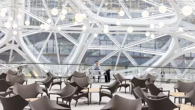 明るいガラスホールの中に座る男性。その手前にたくさんのテーブルと椅子のセットが並んでいる