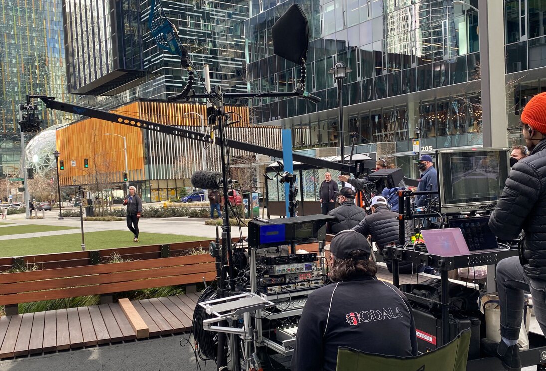 An image of a film crew filming an employee walking across Amazon's campus for the AWS commercial featuring employees.