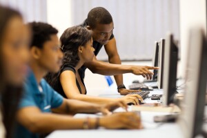 A photo of four students working in a computer lab, sitting in front of desktop computers.