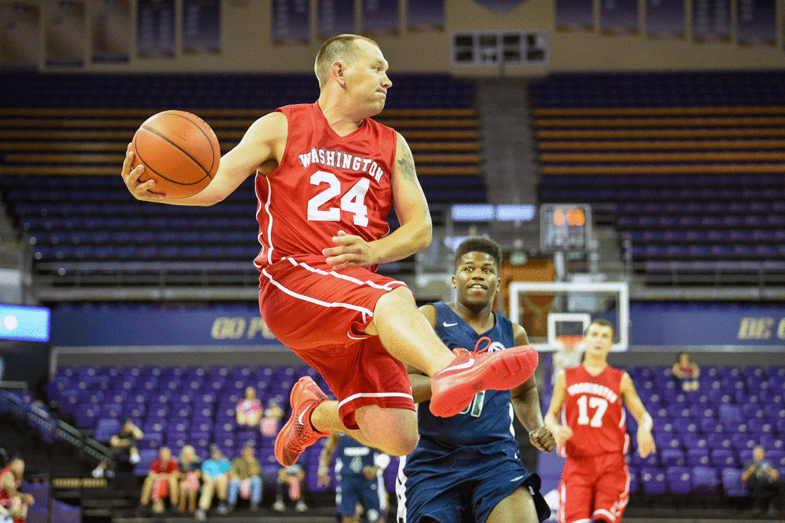 An image of a basketball player jumping with a ball in their hand during the 2022 Special Olympics. There are other players in the background running toward them.