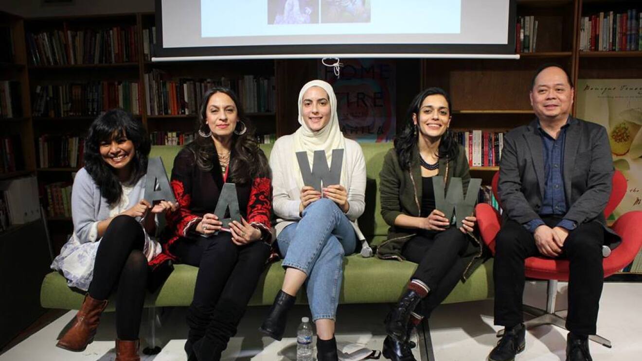 Four women sit on a sofa, holding letters "AAWW," at an Asian American Writer's Workshop. To the right, a male is also shown.  