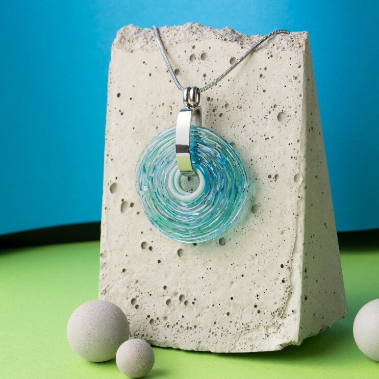 Über einem Steinbehälter hängt ein Kettenanhänger in blauem Glas.