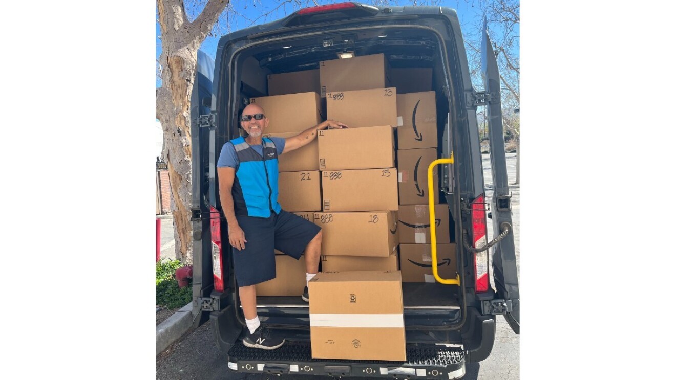 An Amazon employee smiles as he stands in a delivery van filled with boxes of shoes.