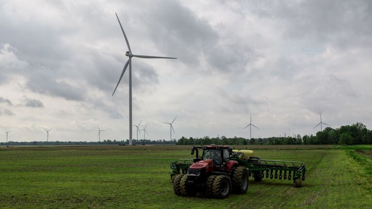 Farming on Delta Wind site with wind turbines and tractor in agricultural field under cloudy sky