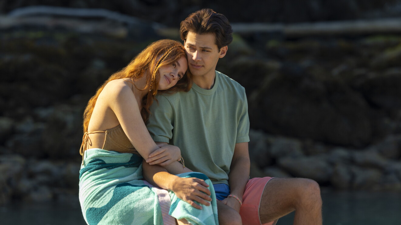 Couple embracing while sitting on rocks by the water at sunset