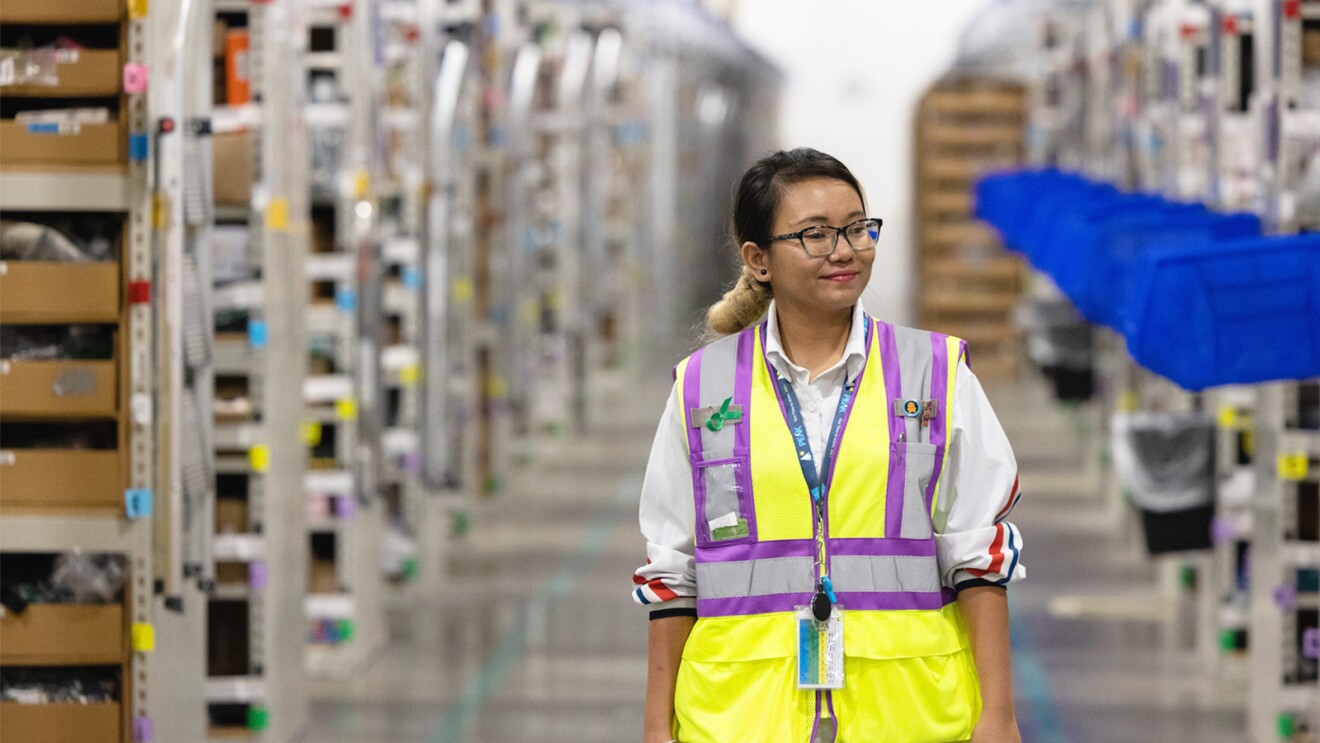 A women wears a yellow safety vest and works in an Amazon fulfillment center.