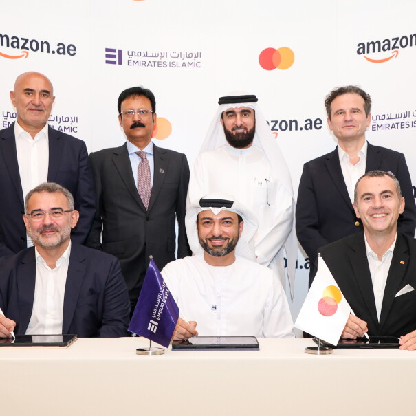Amazon, Mastercard, EIB employees proudly sign a partnership in front of a cobranded rollup