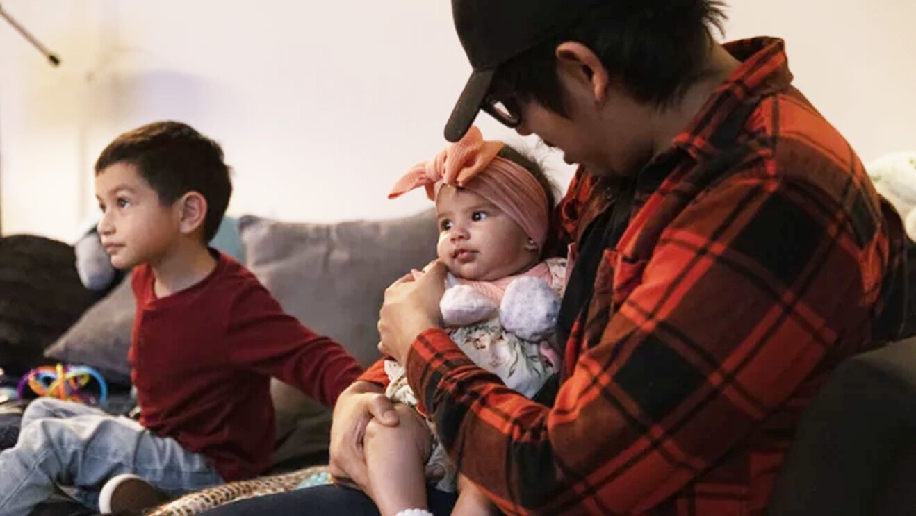A man holds a baby while sitting with a child on a couch.
