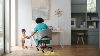 A woman sits at a desk, helping her toddler. On her desk is an Eero device.