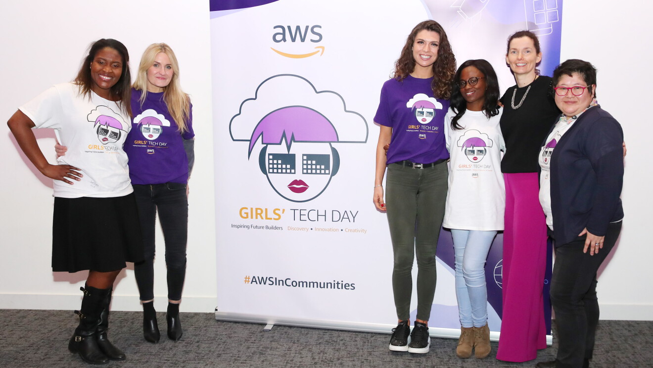 AWS InCommunities - Participating ladies and representatives of AWS standing in front of the AWSInCommunities Girls' Tech Day roll-up at an AWS InCommunity event