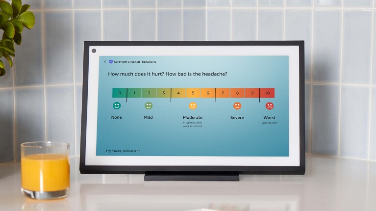 An image showing an Echo Show device sitting on a kitchen counter next to a cup of orange juice. The screen is showing the new "symptom checker" feature.