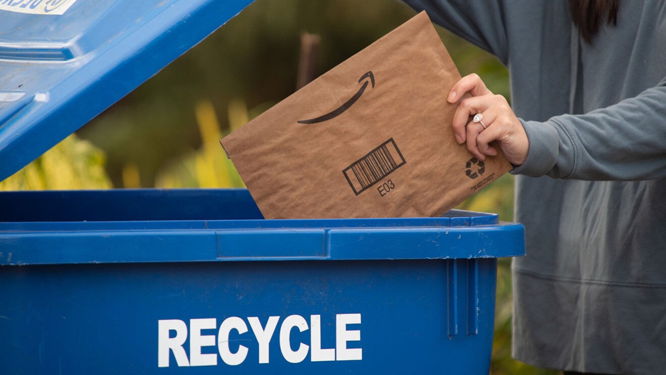 La mano de una mujer tirando un sobre de cartón de Amazon en el contenedor azul de papel. 