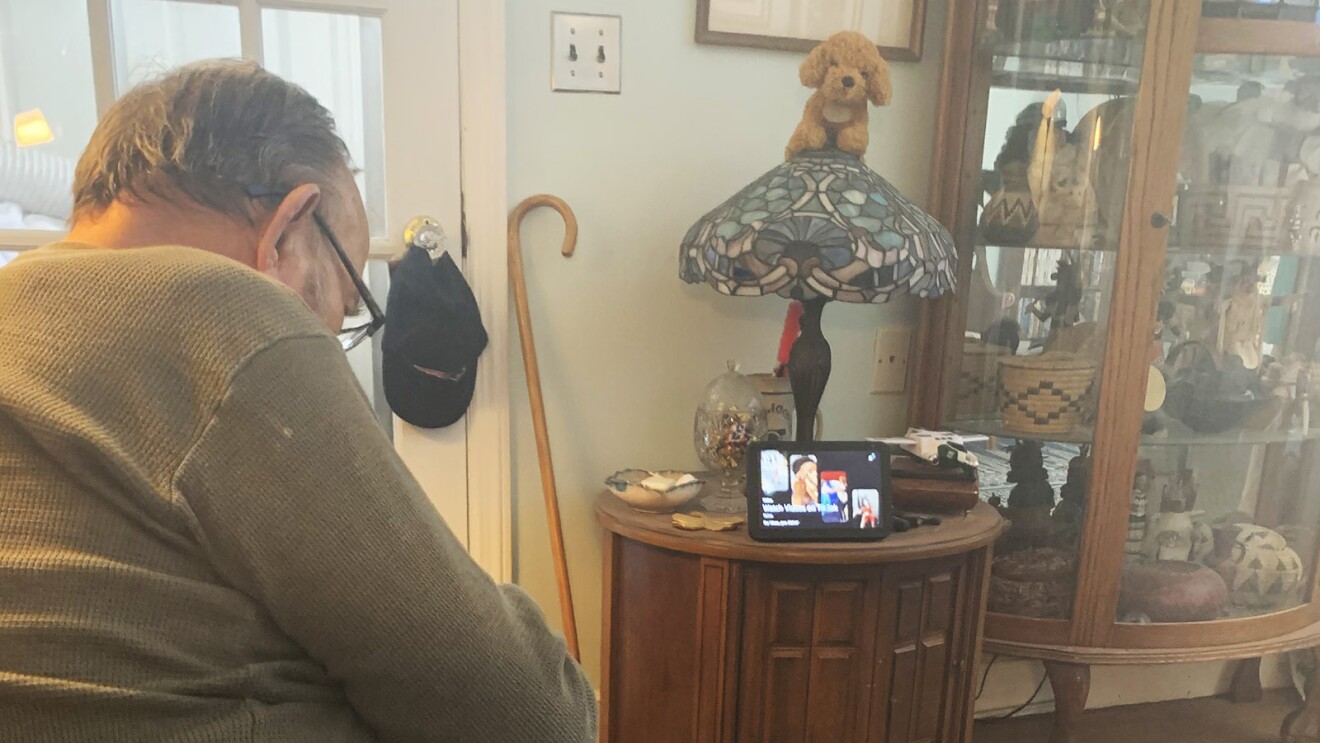 An image of a man sitting on his couch looking at his Echo Show device in the background.