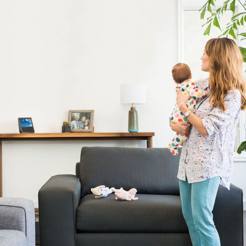 An Amazon Echo Show on a console table in a home with a mom and baby.