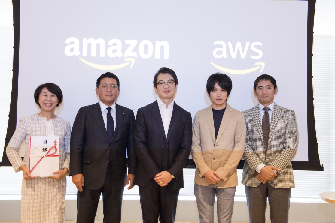 スクリーンの前に並んで立つ5人の人物。スクリーンには「amazon」と「aws」のロゴが映っている。