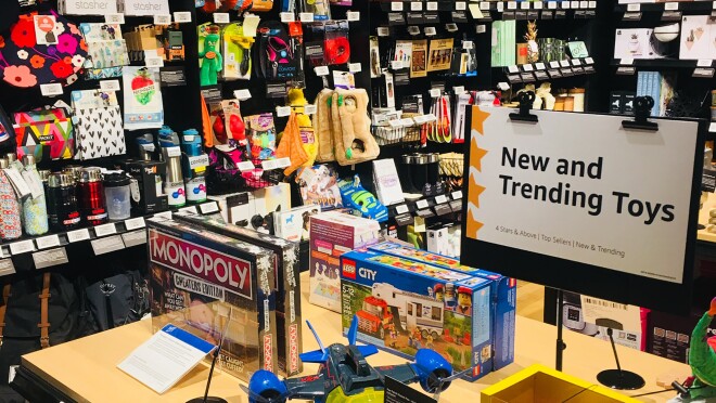 亚马逊四星级商店里的一桌子“新玩具和流行玩具”。桌上放着大富翁棋盘游戏、乐高城市套装和COZMO机器人玩具。每件产品都有一个数字价签和客户评论。桌子后面是给宠物的礼物、给大人的礼物、蜡烛和家庭装饰品。