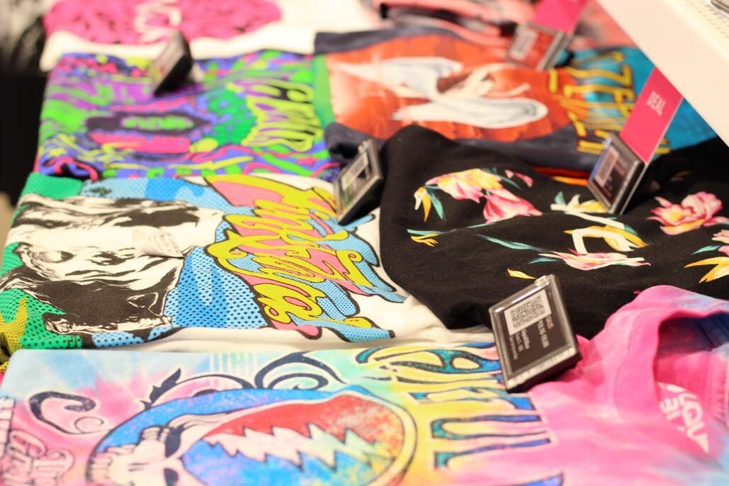 A stack of colorful graphic tee shirts folded and laid on a shelf at a store.
