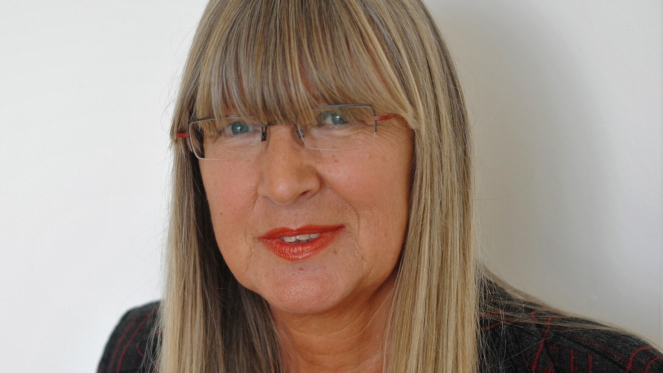 Eine Frau mit blonden langen Harren und Brille lächelt in die Kamera. Sie trägt roten LIppenstift.