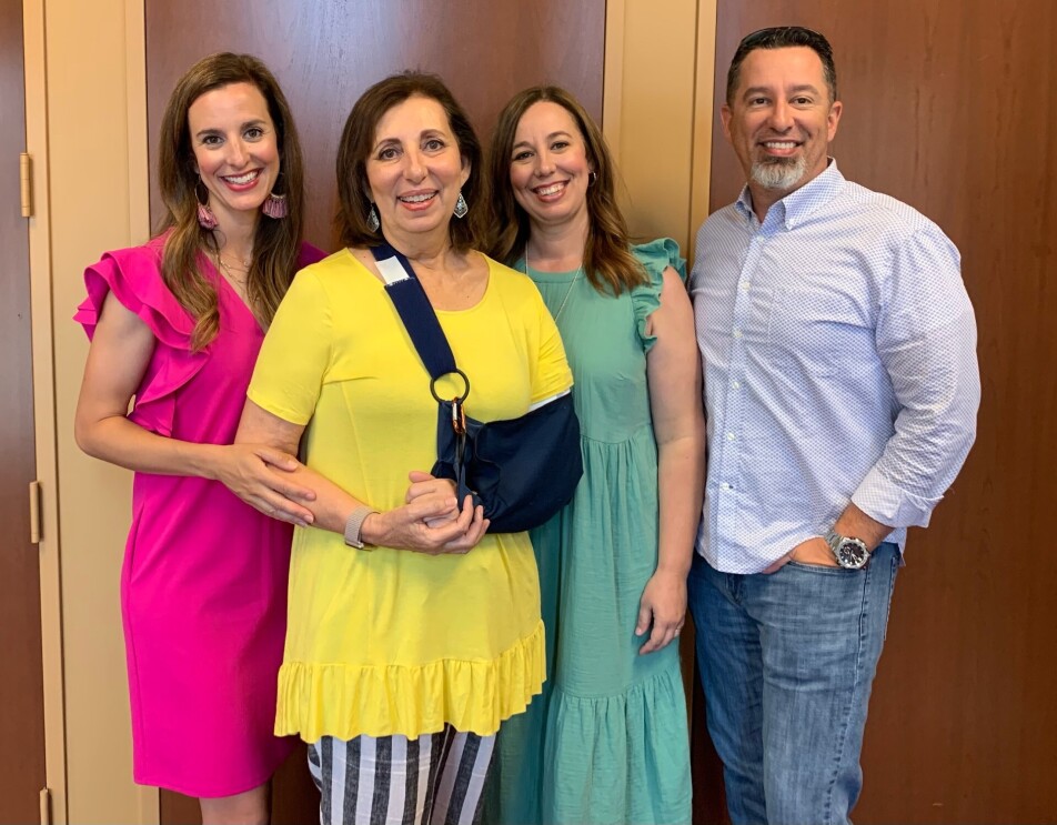 Rebecca wears a sling supporting her left arm while her, her two daughter, and son smile for the camera.