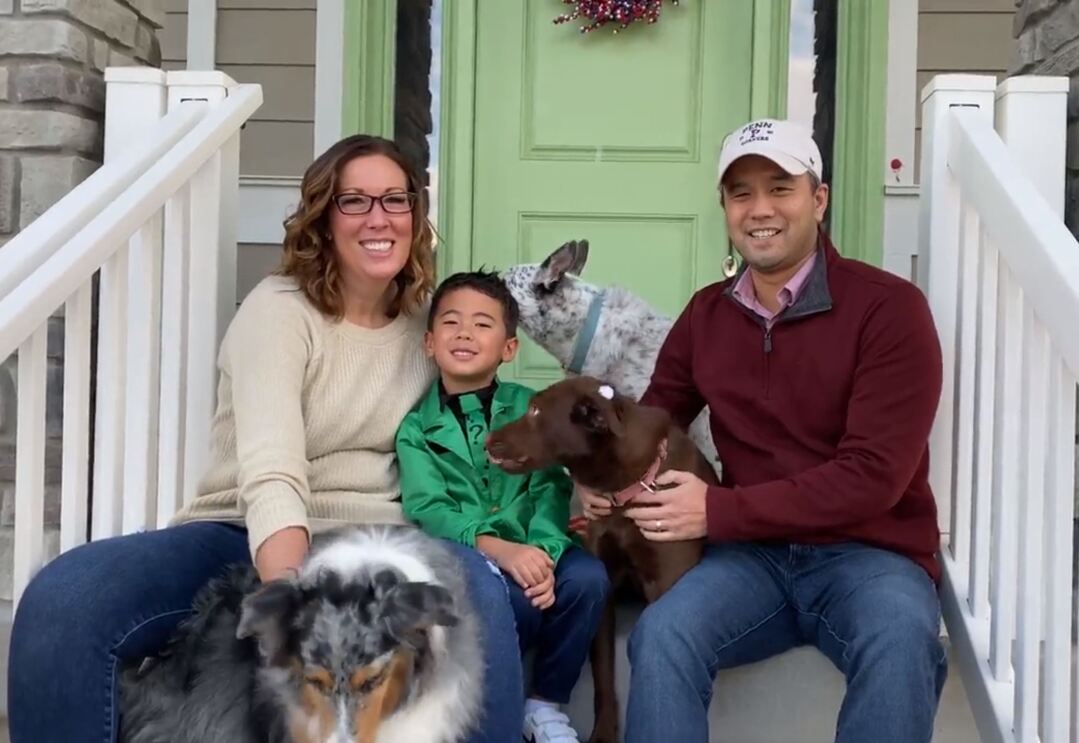 Aman and woman sit with their child and three dogs.