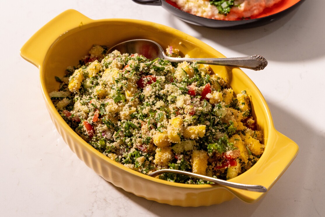 An image of a yellow bowl with fonio grain and vegetables in it. There are two spoons in the mixture ready to serve.
