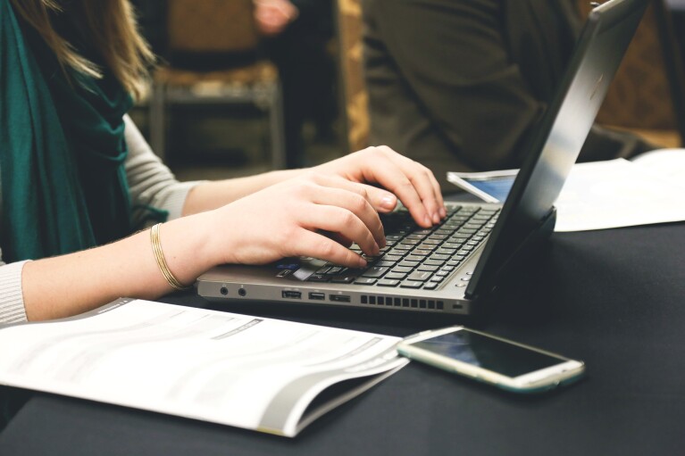 Woman working on a laptop computer, her hands are posed over the keyboard of the device.
