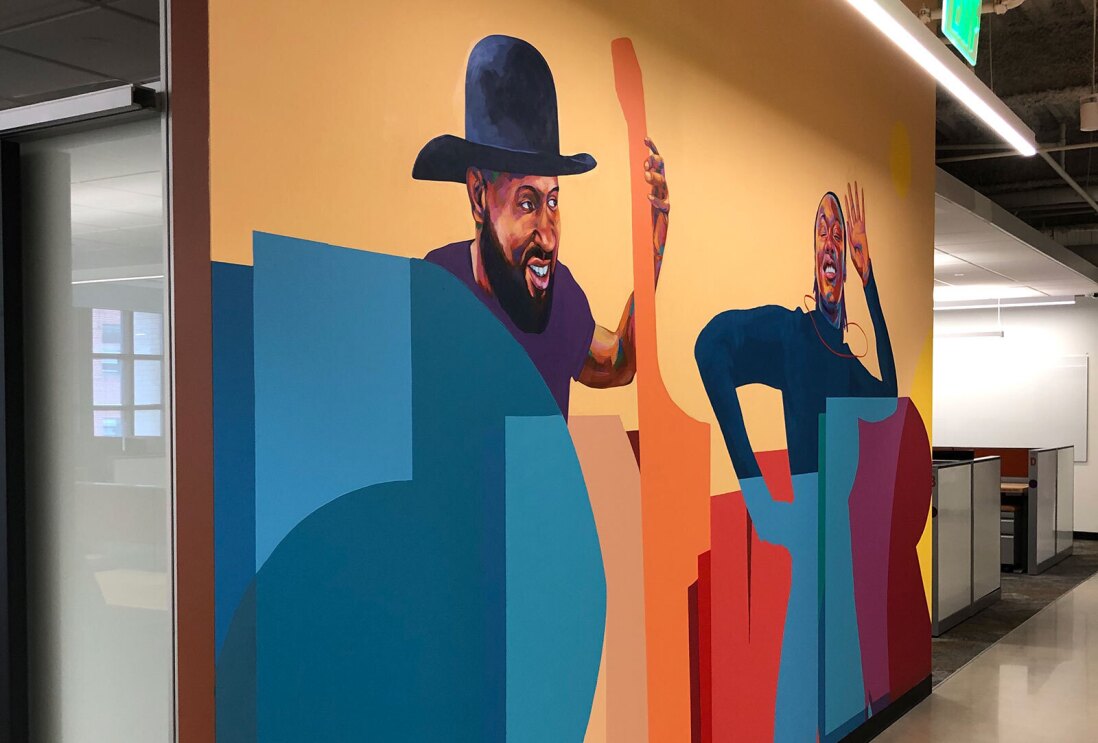 An image of a painted mural showing two people smiling and lettering at the Amazon Denver office.