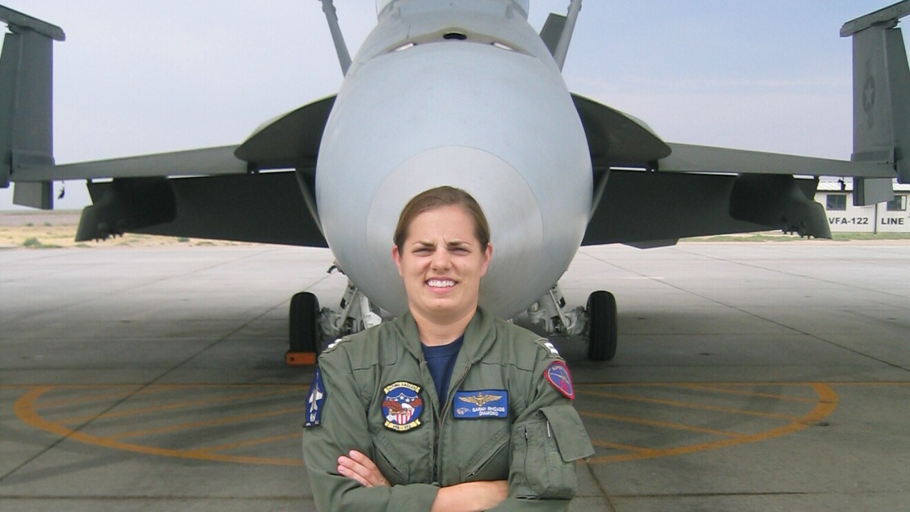 一个女人在美国海军战斗机的飞行服站在面前她双手交叉。