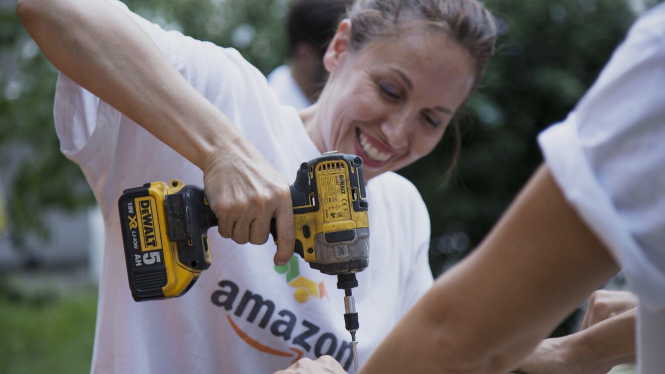 Volontaria di Amazon sorride in primo piano mentre regge un trapano durante i lavori alla Scuola Media Leonardo da Vinci di Affori, nella periferia di Milano.