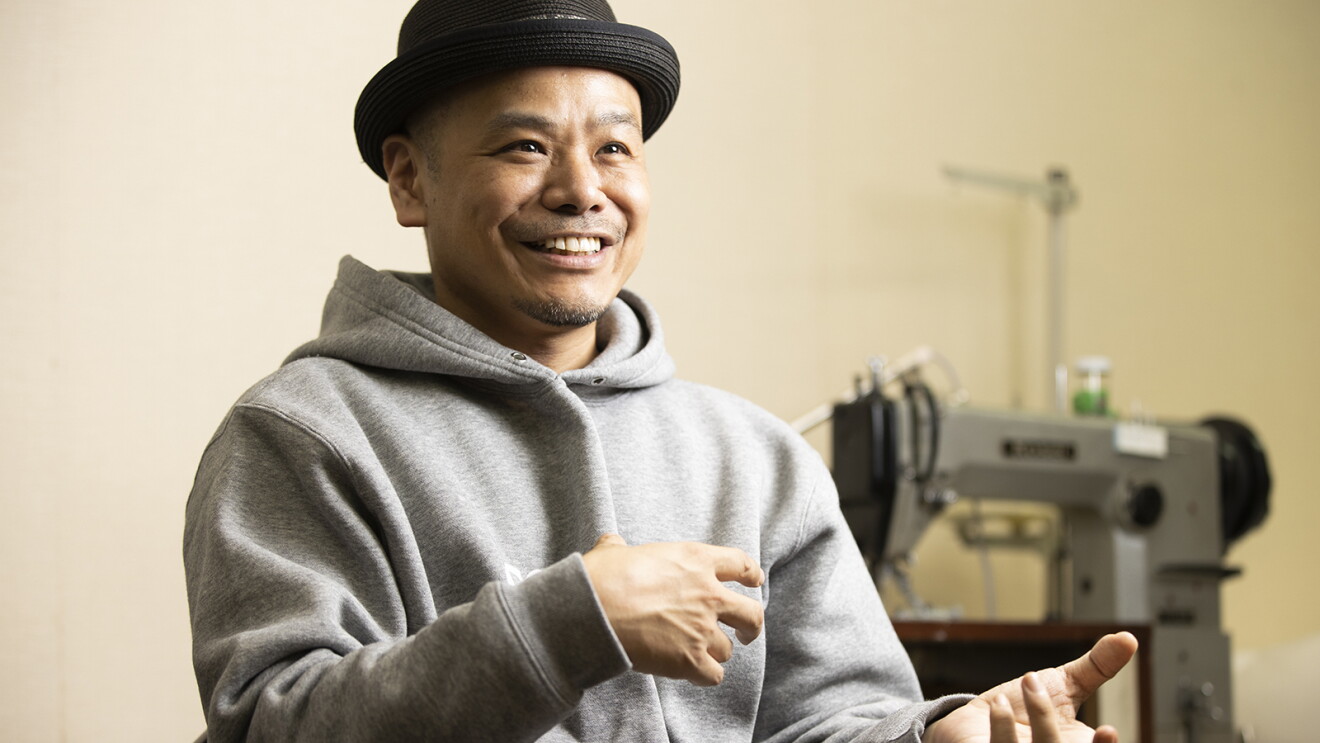 ミシンのある作業場で、嬉しそうに話す竜田さんの写真